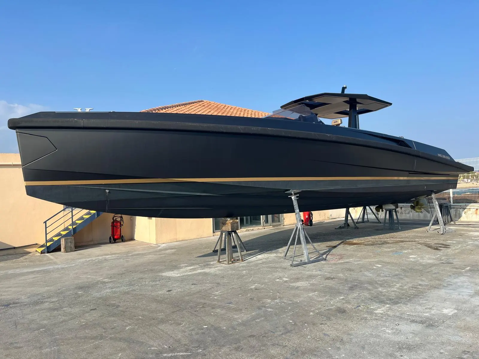 Wally 48 — Bateau noir à bande dorée présenté à terre sur bers, vu de profil.