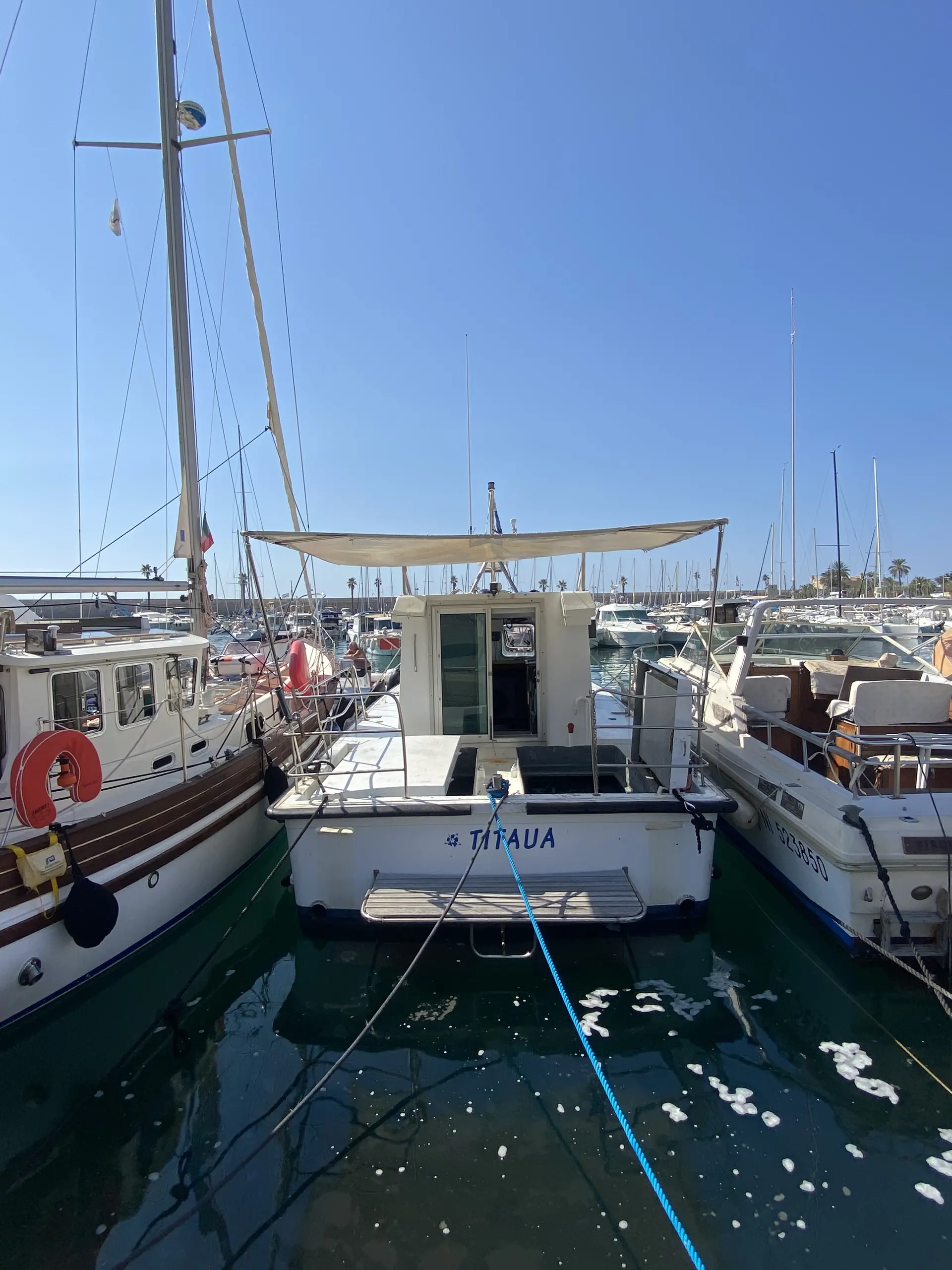Polymer Vedette — Vue arrière d’un voilier amarré dans un port, entouré d’autres bateaux.