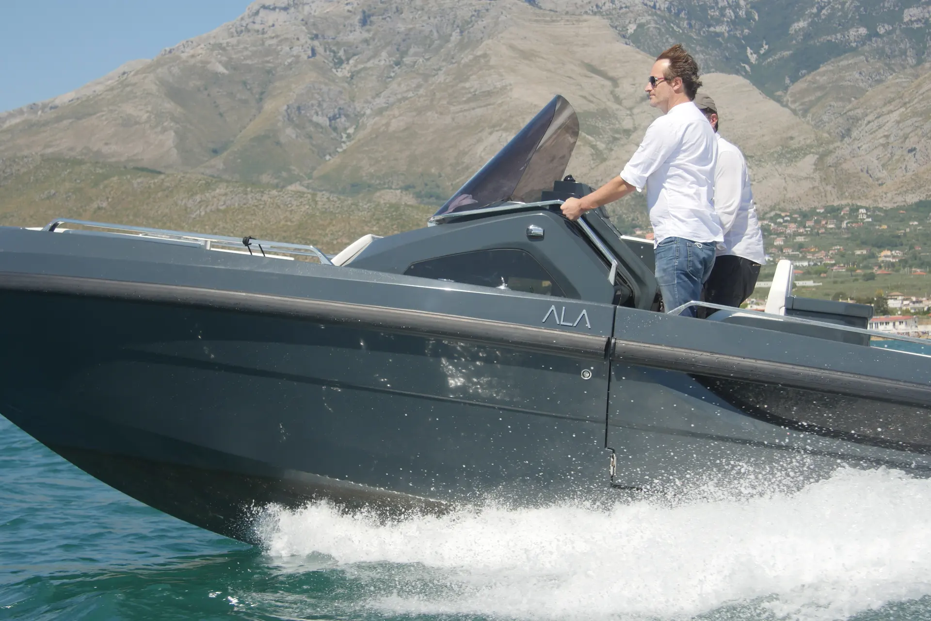 Ala Yacht Ala 8 — Bateau à moteur en navigation devant un relief montagneux, avec deux personnes à bord.
