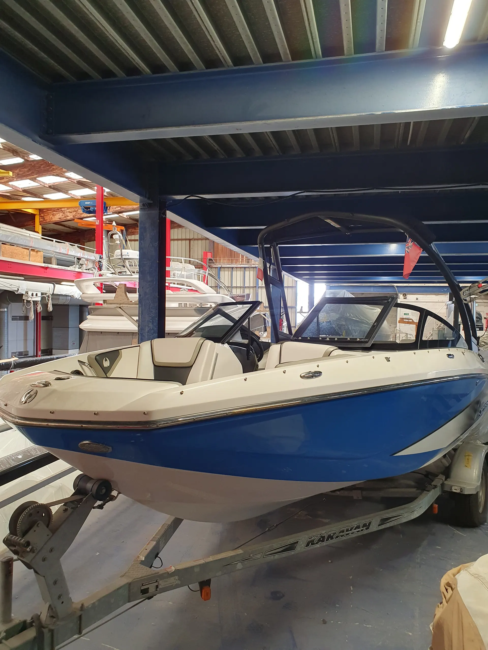 Scarab Boats Scarab 195 Impulse — Bateau à coque bleue photographié sur sa remorque dans un hangar.