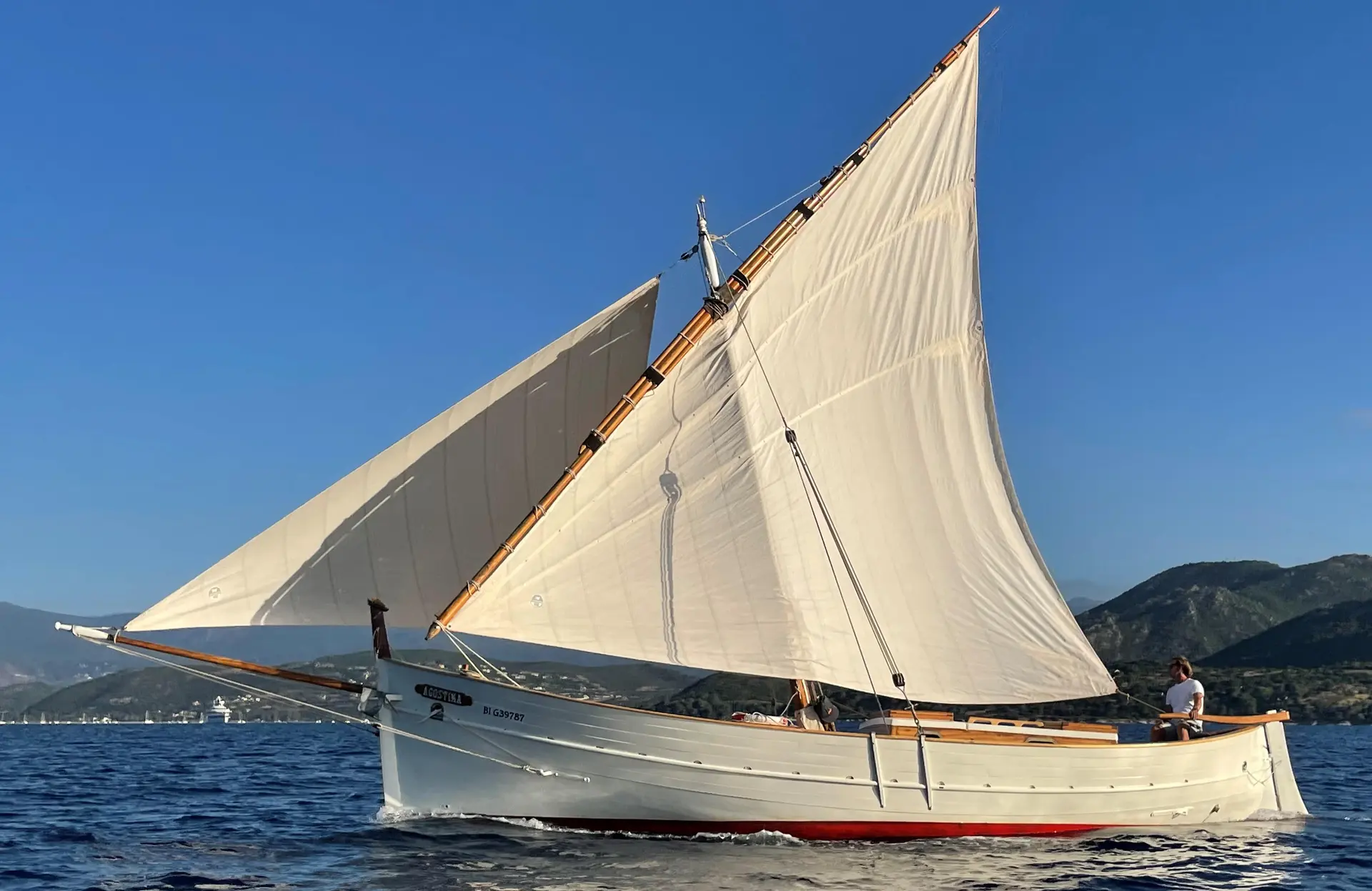 Cantiere Sangermani Rivaneto Ligure — Voilier classique à deux voiles naviguant près d’une côte montagneuse.