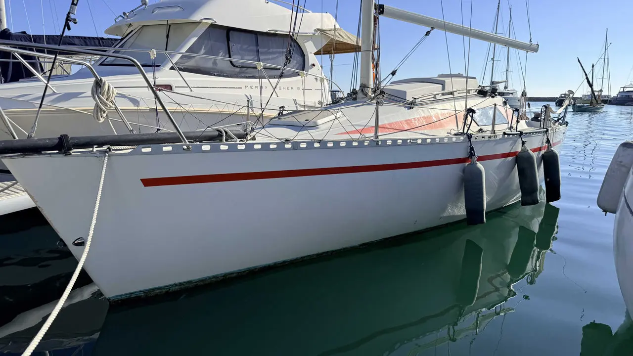 Comar Yachts Comet 28 — Voilier blanc à bande rouge amarré dans une marina, vu de profil.