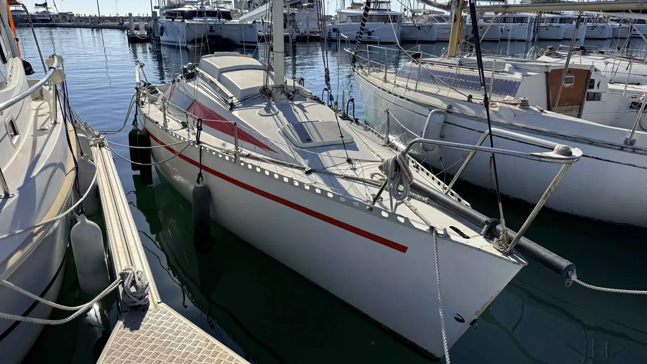 Comar Yachts Comet 28 — Voilier blanc à bandes rouges amarré dans un port de plaisance.