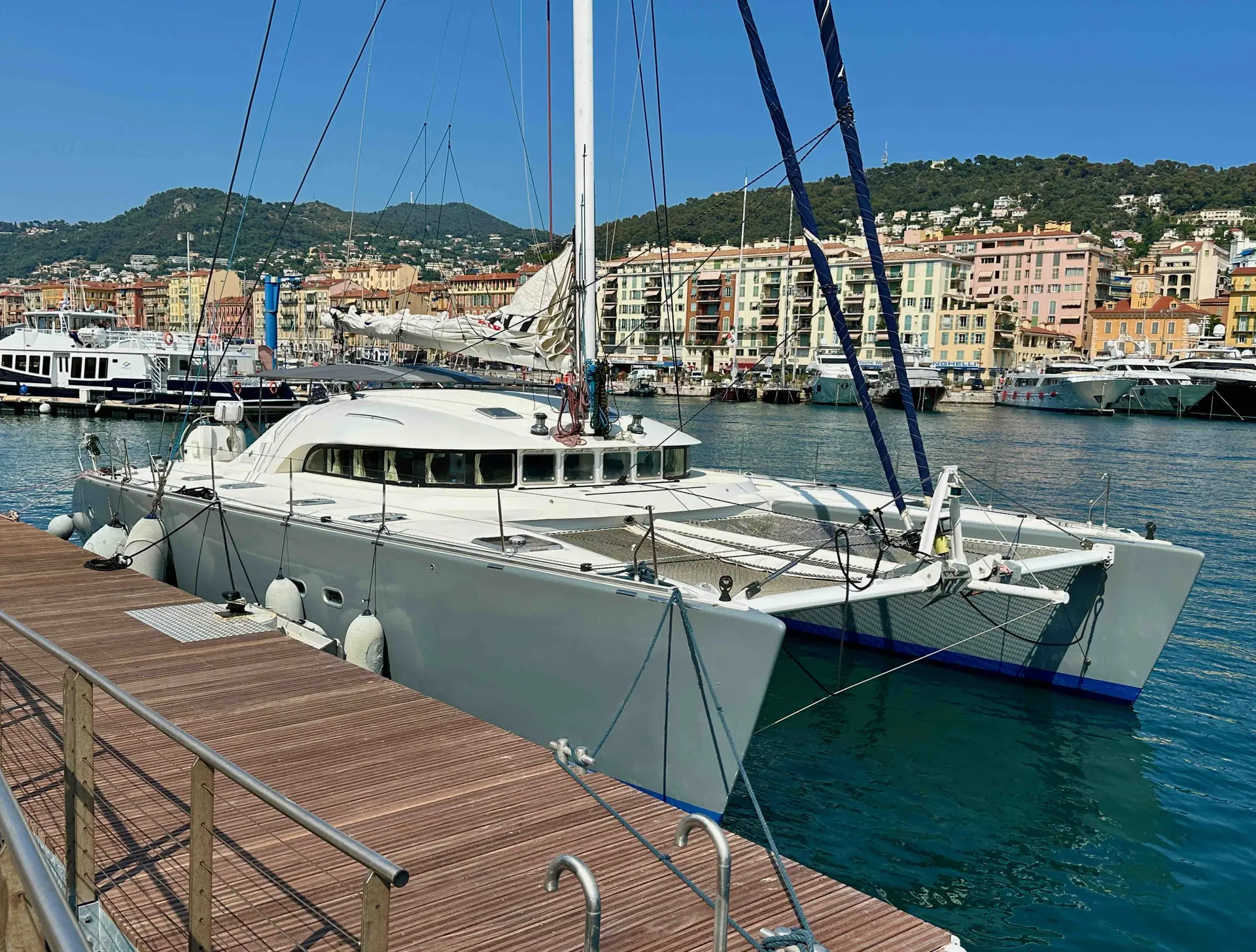 Cnb LAGOON 570 — Catamaran blanc amarré dans un port méditerranéen, avec la ville en arrière-plan.