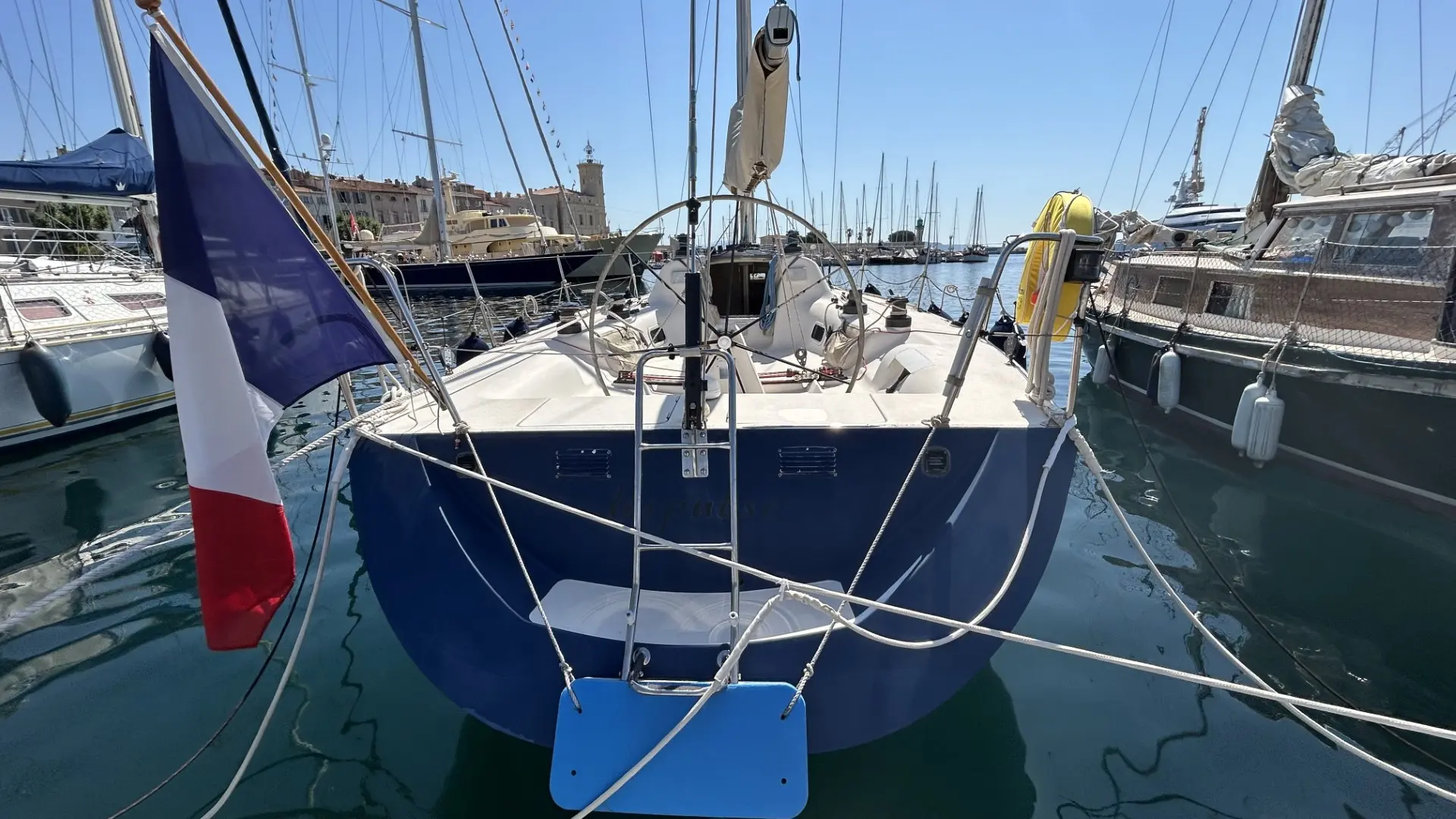 X-Yachts IMX 38 — Vue arrière d’un voilier amarré dans un port, avec pavillon tricolore.