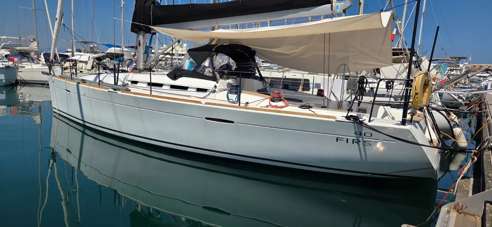 Beneteau First 40 — Voilier blanc amarré dans une marina, vu de trois quarts côté tribord.