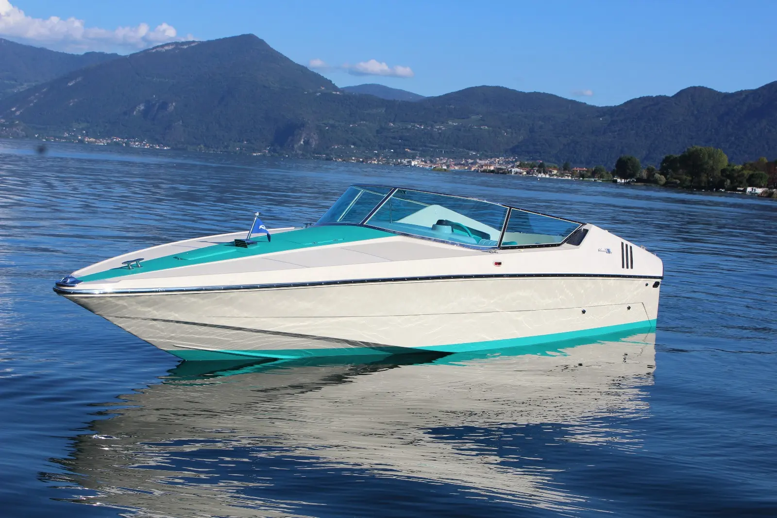 Riva Saint Tropez — Bateau à moteur blanc et turquoise vu de profil sur un lac montagneux.