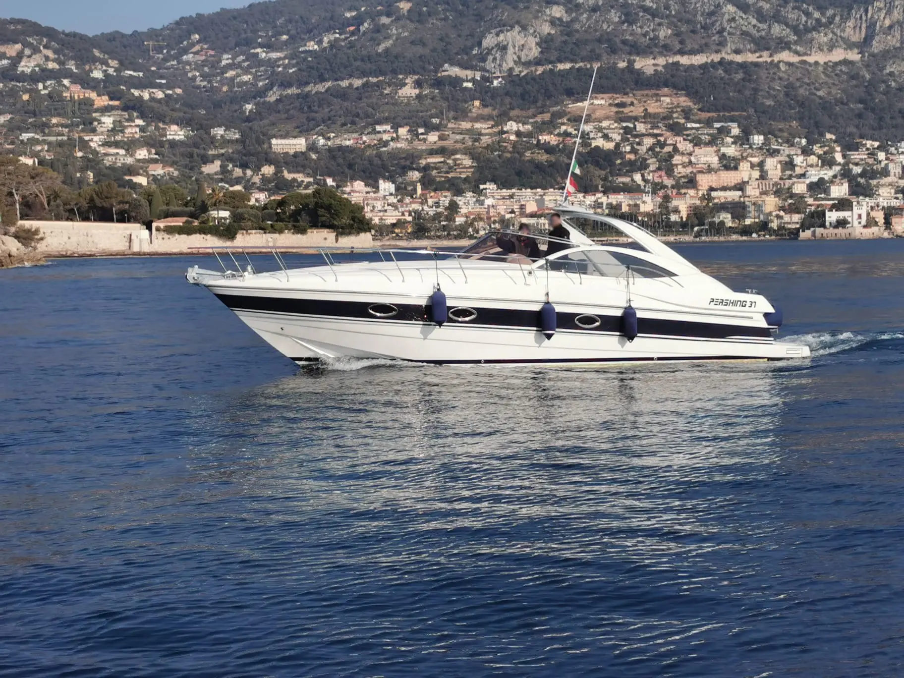 Pershing 37 — Bateau à moteur blanc et noir naviguant le long d'une côte urbanisée.