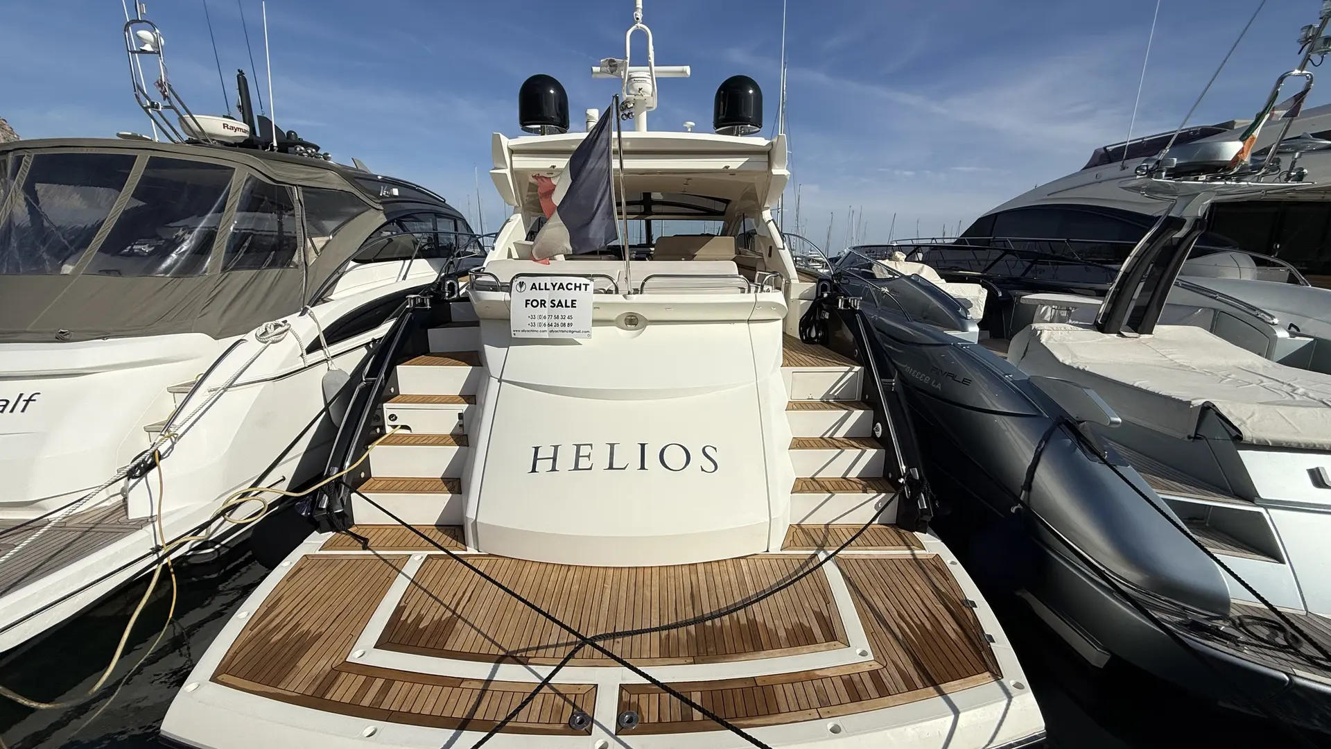 Sunseeker Predator 60 — Vue arrière d’un yacht blanc nommé HELIOS, amarré entre deux autres bateaux.