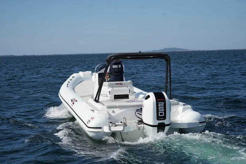 4XC HA27 — Bateau semi-rigide blanc naviguant sur une mer agitée, vu de trois quarts arrière.