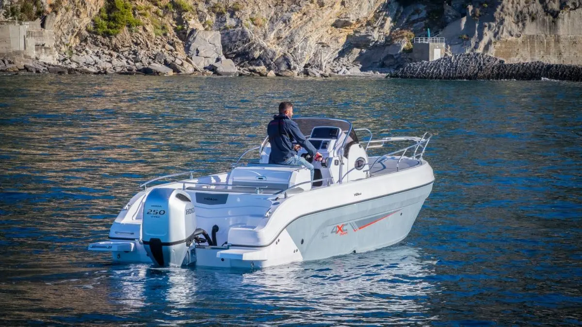 4XC H26SD — Bateau à moteur vu de trois quarts arrière, naviguant près d'une côte rocheuse.