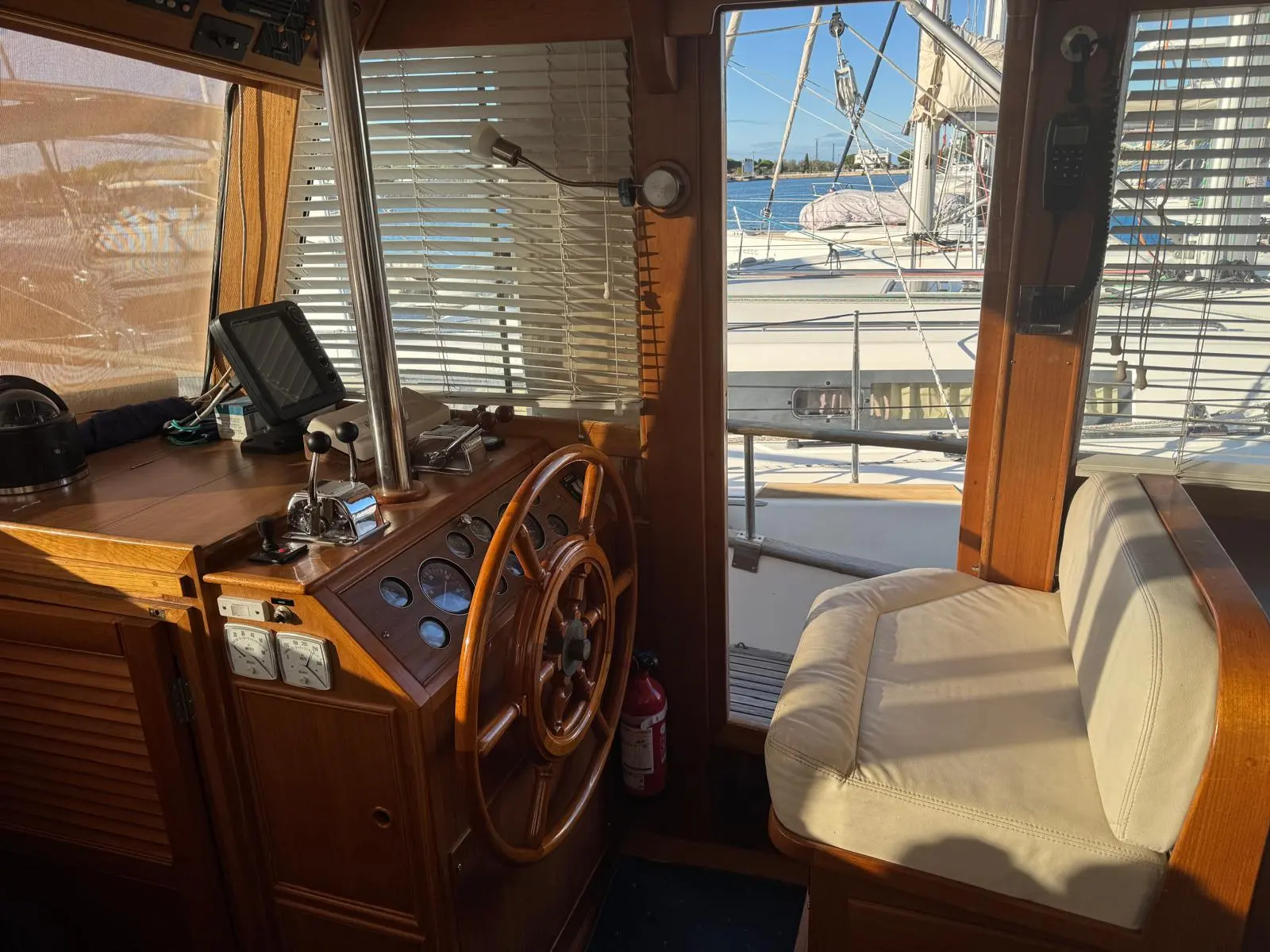 Grand Banks MY 42 — Poste de pilotage intérieur avec volant, commandes et siège, vue sur le pont.