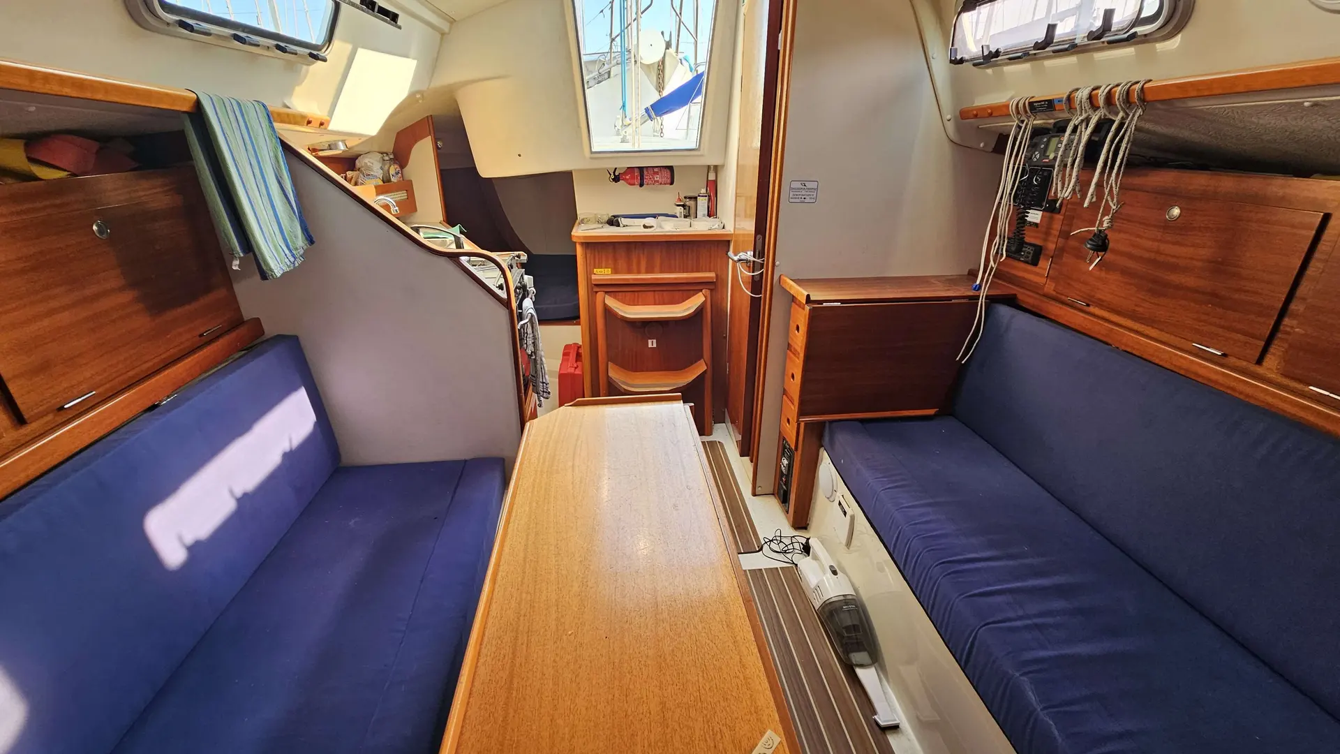 Hanse 300 — Carré intérieur d’un voilier avec banquettes, table et rangements en bois.