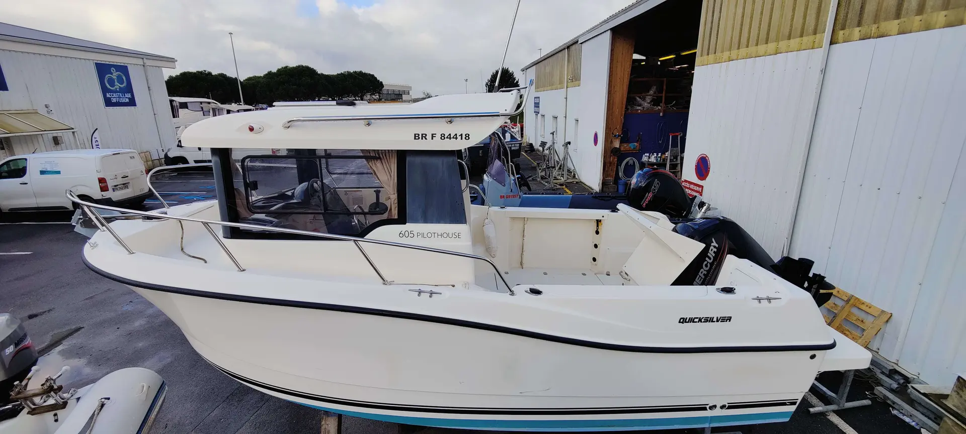 Quicksilver Captur 605 Pilothouse — Bateau à moteur blanc photographié devant un hangar nautique.