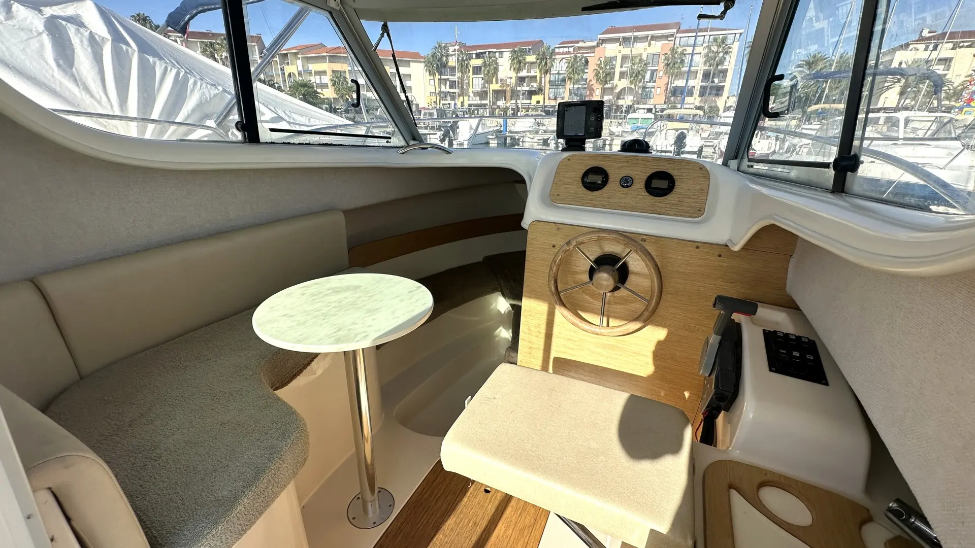 Sessa Marine Dorado 22 — Poste de pilotage intérieur avec banquette, table et vue sur la marina.