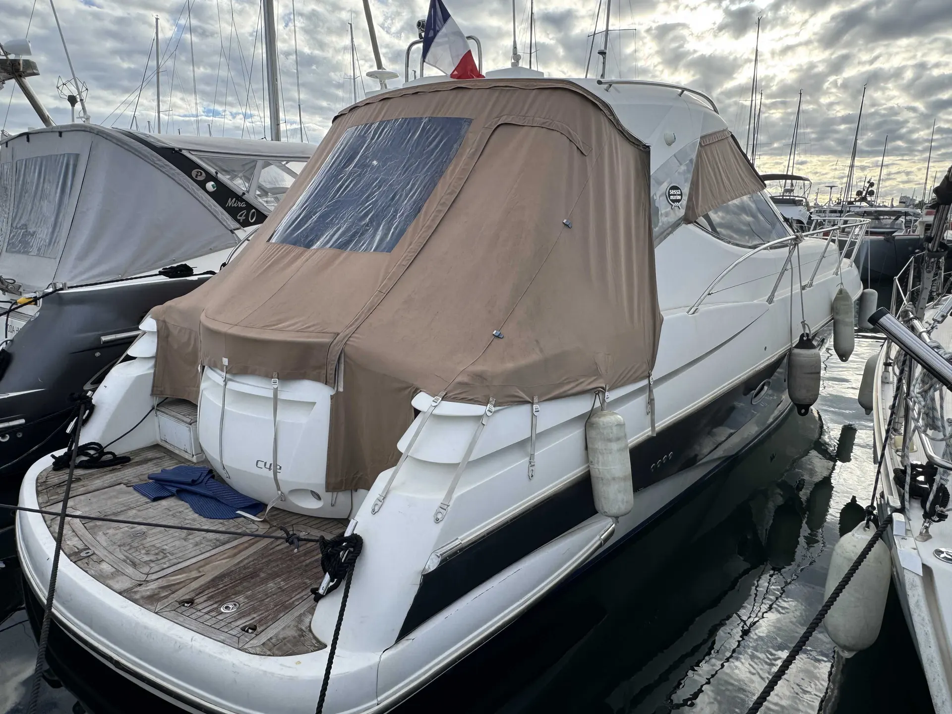 Sessa Marine C42 — Bateau à moteur vu de trois quarts arrière dans un port, capote beige déployée.