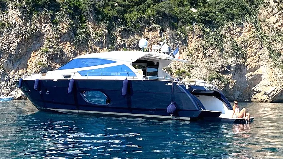 Cayman 57 HT — Bateau à moteur bleu amarré devant une côte rocheuse, avec une personne à l’arrière.
