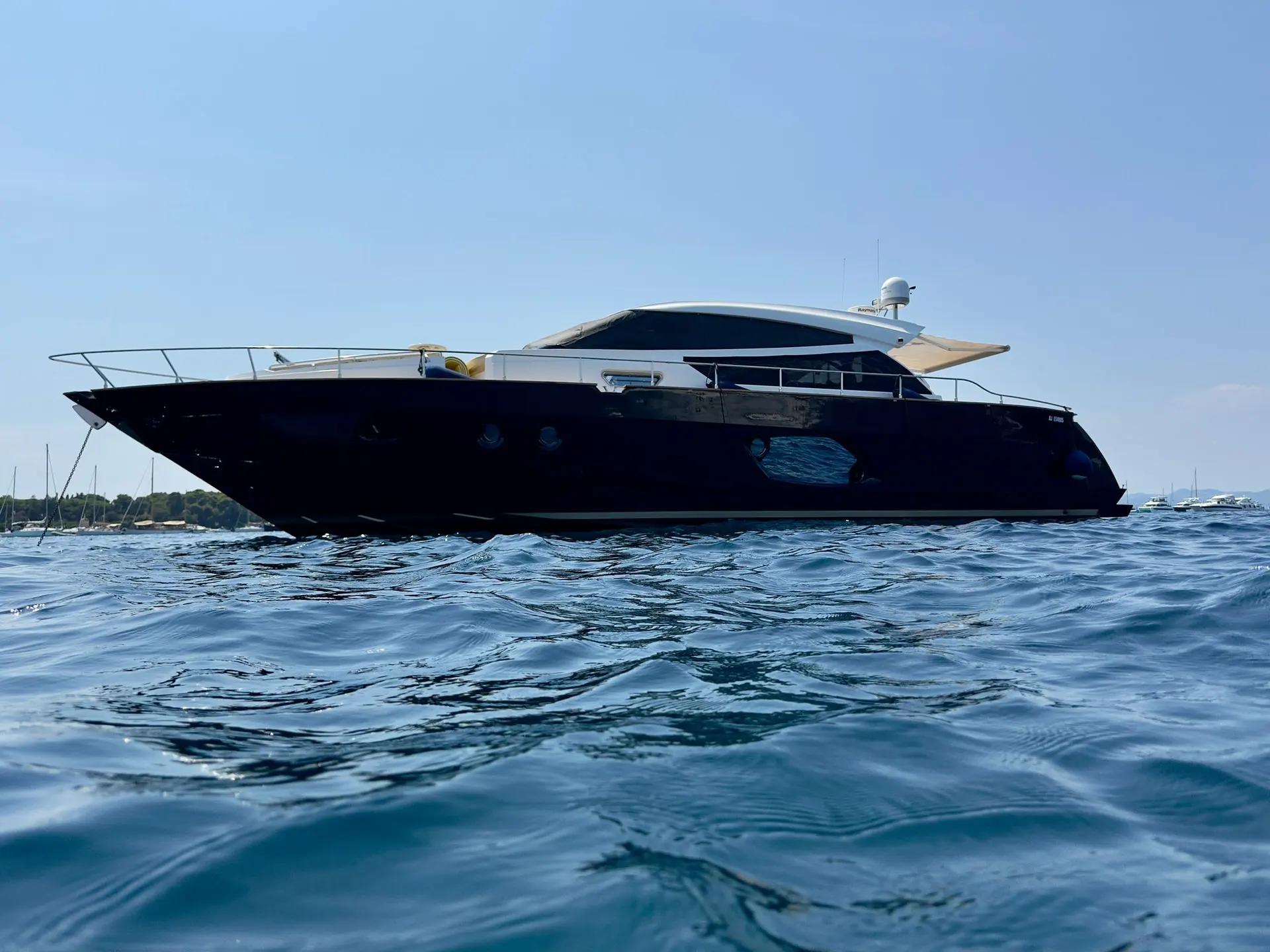 Cayman 57 HT — Vue de profil d’un yacht à moteur noir naviguant sur une baie ensoleillée.