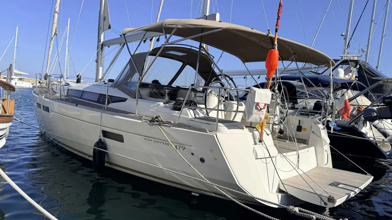 Jeanneau Sun Odyssey 479 — Voilier blanc vu de trois quarts arrière dans une marina, avec bimini déployé.