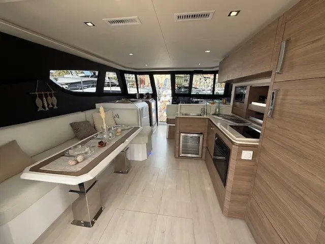 Aventura Catamarans Aventura 38 — Vue du carré et de la cuisine d’un catamaran, avec salon, table et équipements intégrés.