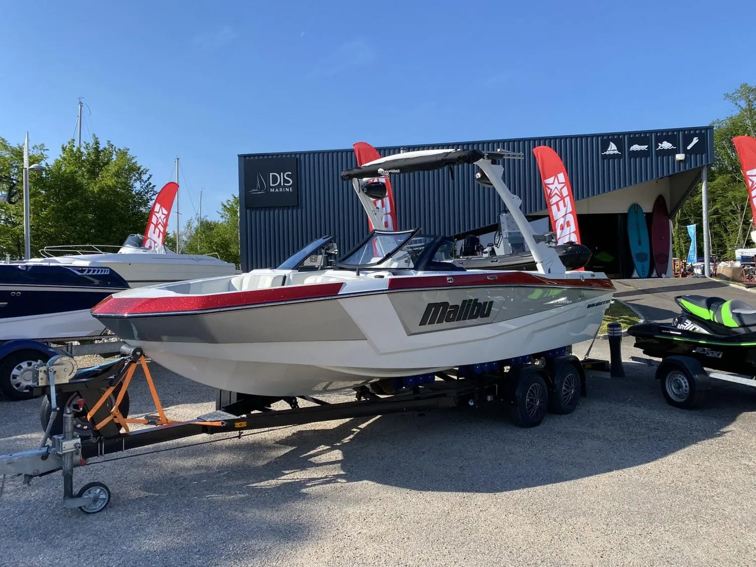 Malibu Wakesetter 21 VLX — Bateau à moteur rouge et blanc sur remorque devant un bâtiment nautique.