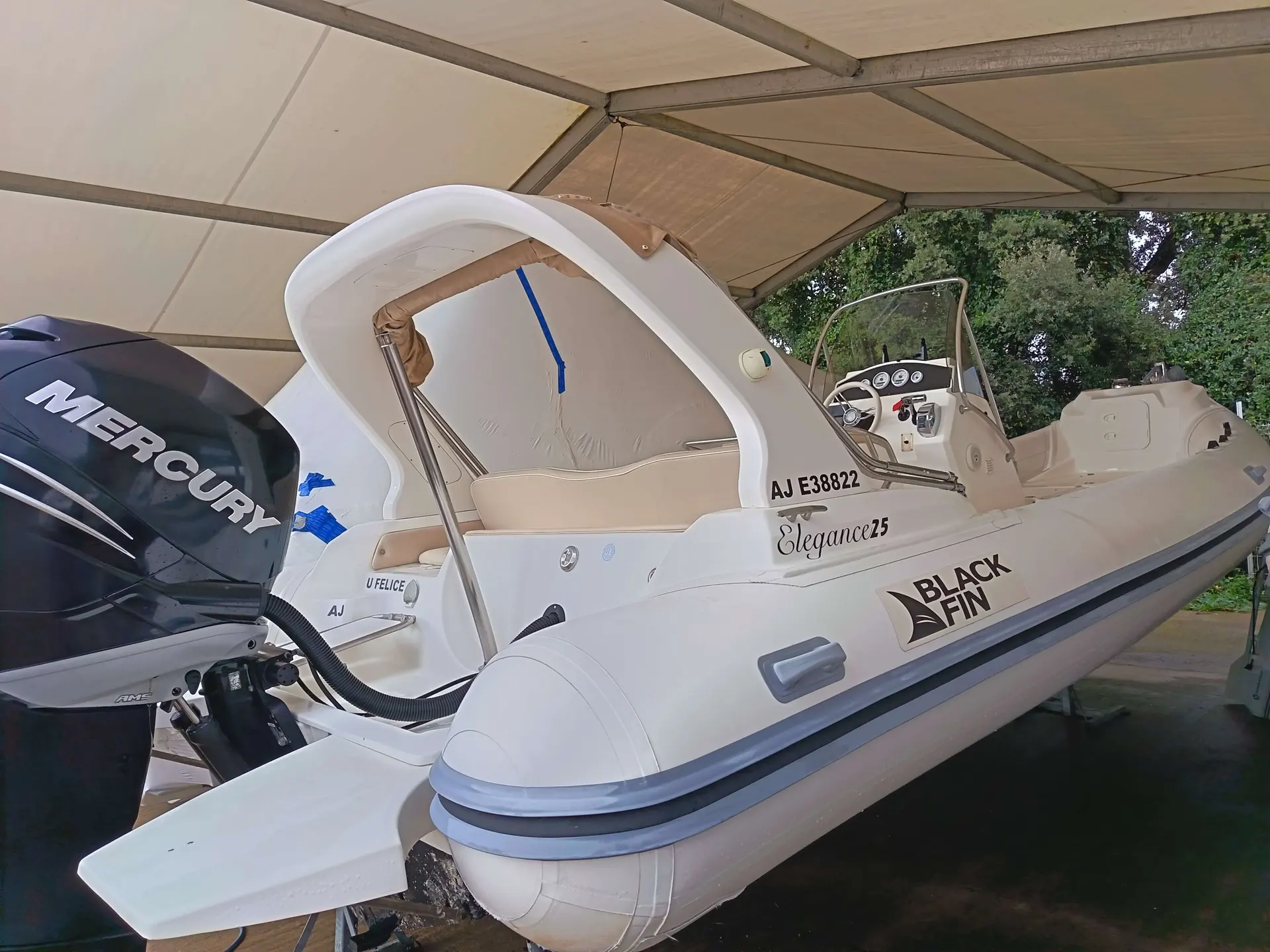 Black Fin 25 — Bateau pneumatique blanc vu de trois quarts sous une couverture, avec moteur hors-bord.