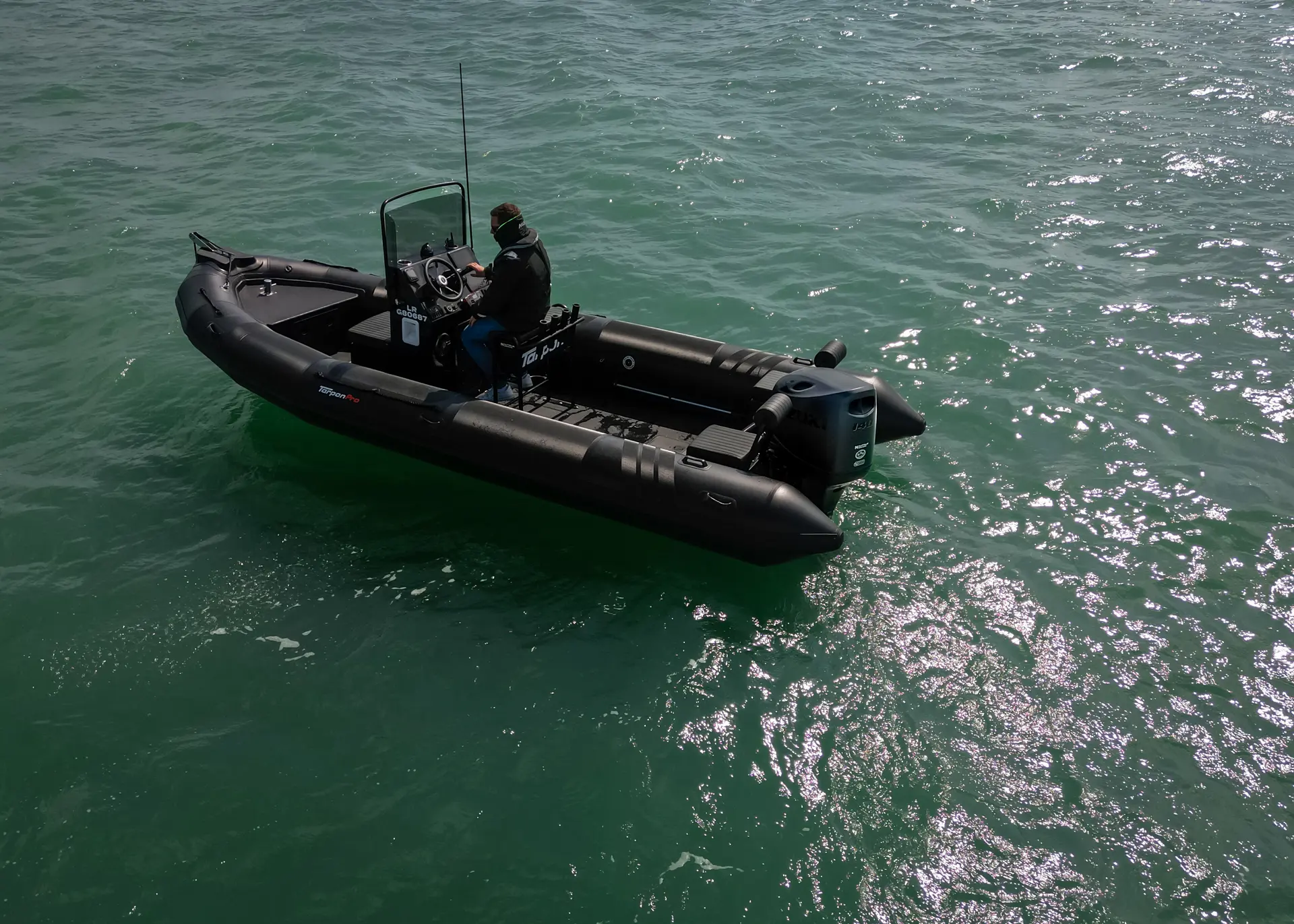 Tarpon DV65 — Bateau pneumatique noir vu de trois quarts sur l’eau, avec une personne à la barre.