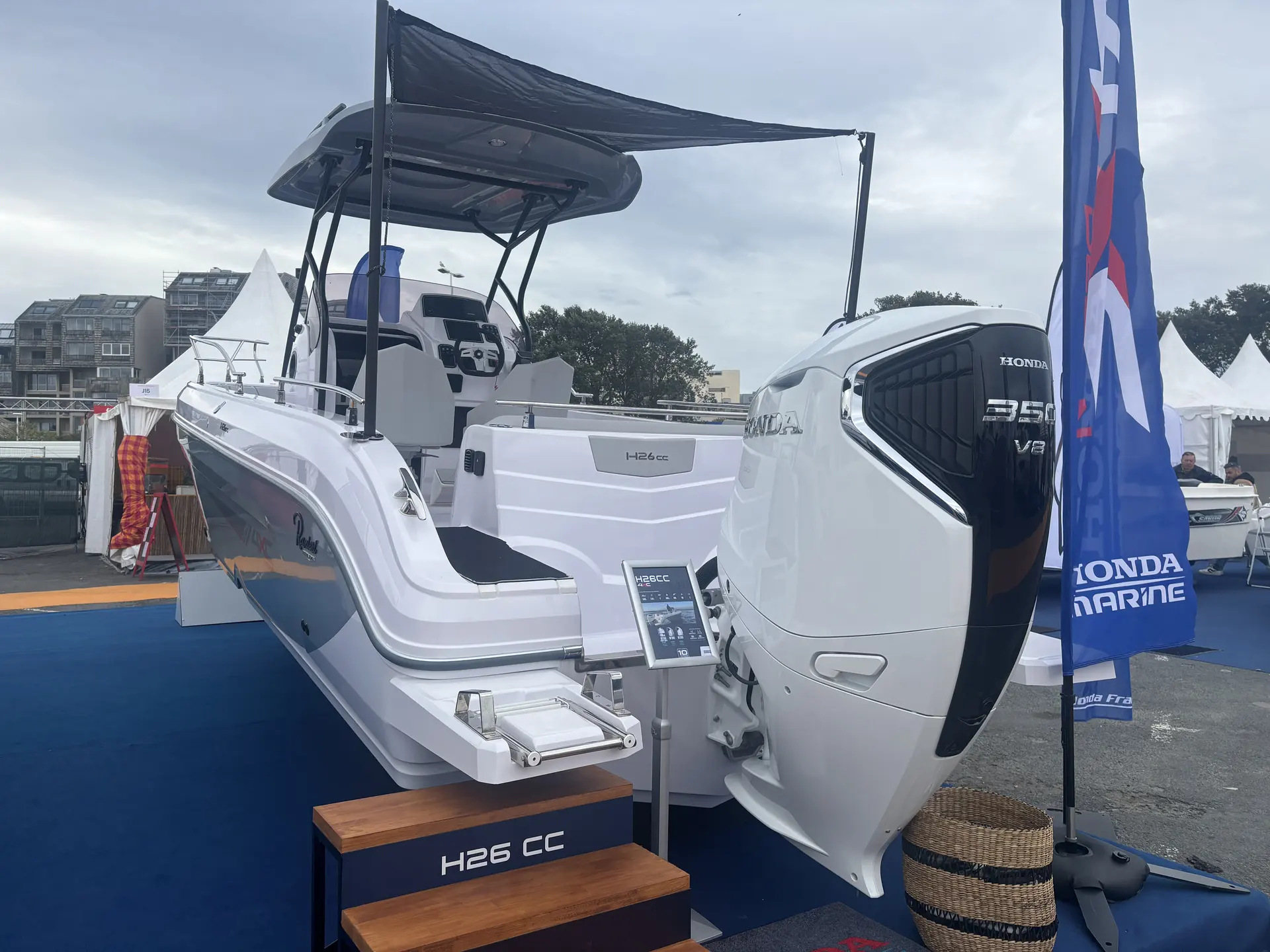 4XC H26CC — Bateau exposé sur un stand, équipé d’un grand moteur hors-bord et d’un taud.