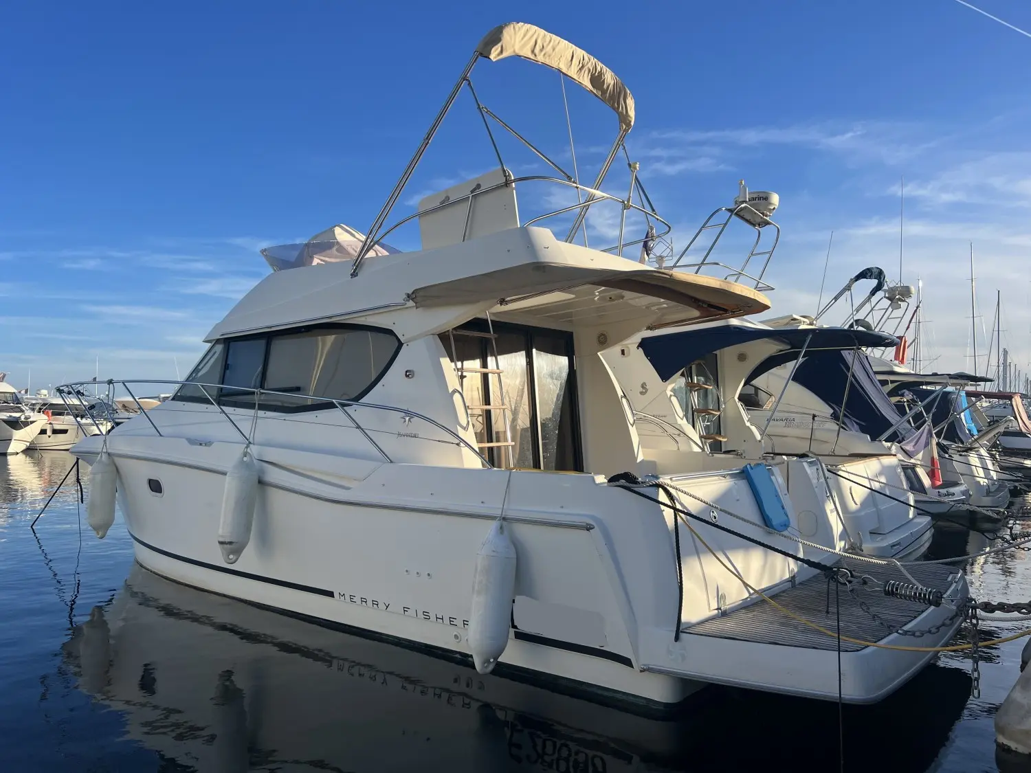 Jeanneau Merry Fisher 10 — Vedette à moteur blanche amarrée dans un port, vue de trois quarts arrière.