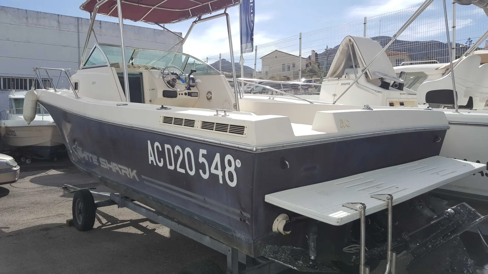 White Shark 237 — Bateau à moteur blanc et gris présenté sur remorque dans un port à sec.