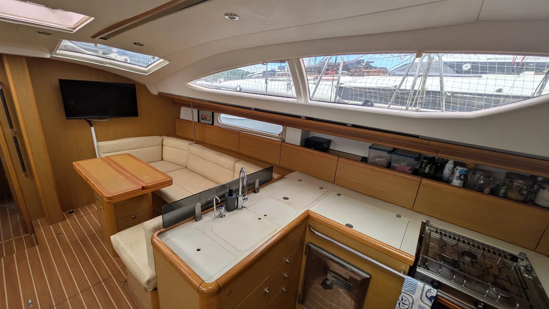 Jeanneau Sun Odyssey 45 DS — Vue intérieure du salon et de la cuisine d’un bateau, avec banquette et table.