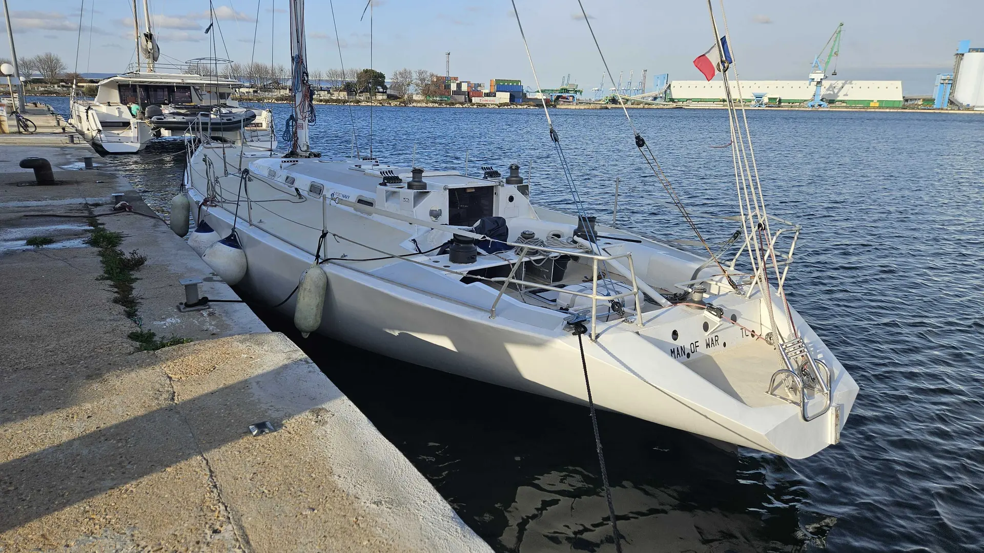 German Frers 48 — Voilier blanc amarré à un quai dans un port industriel.