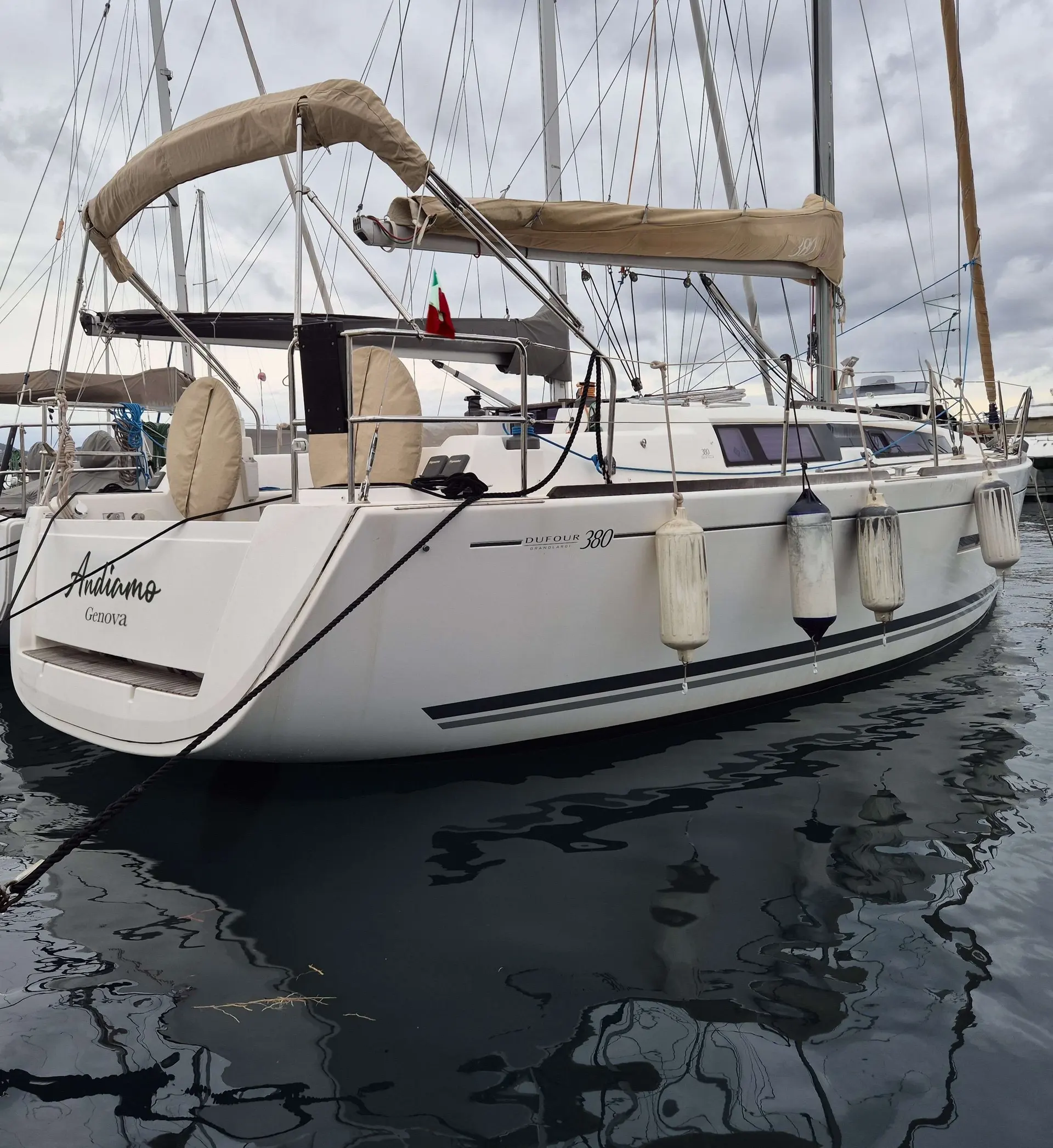 Dufour 380 — Voilier blanc vu de trois quarts arrière dans un port, sous un ciel couvert.