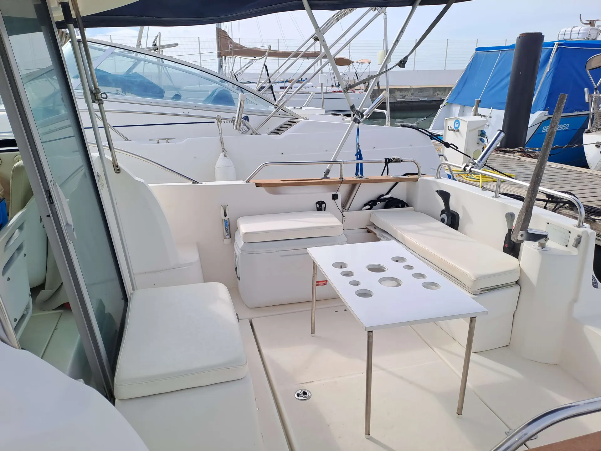 Jeanneau Merry Fisher 705 — Cockpit extérieur avec banquettes, table et poste de pilotage d’un bateau à quai.