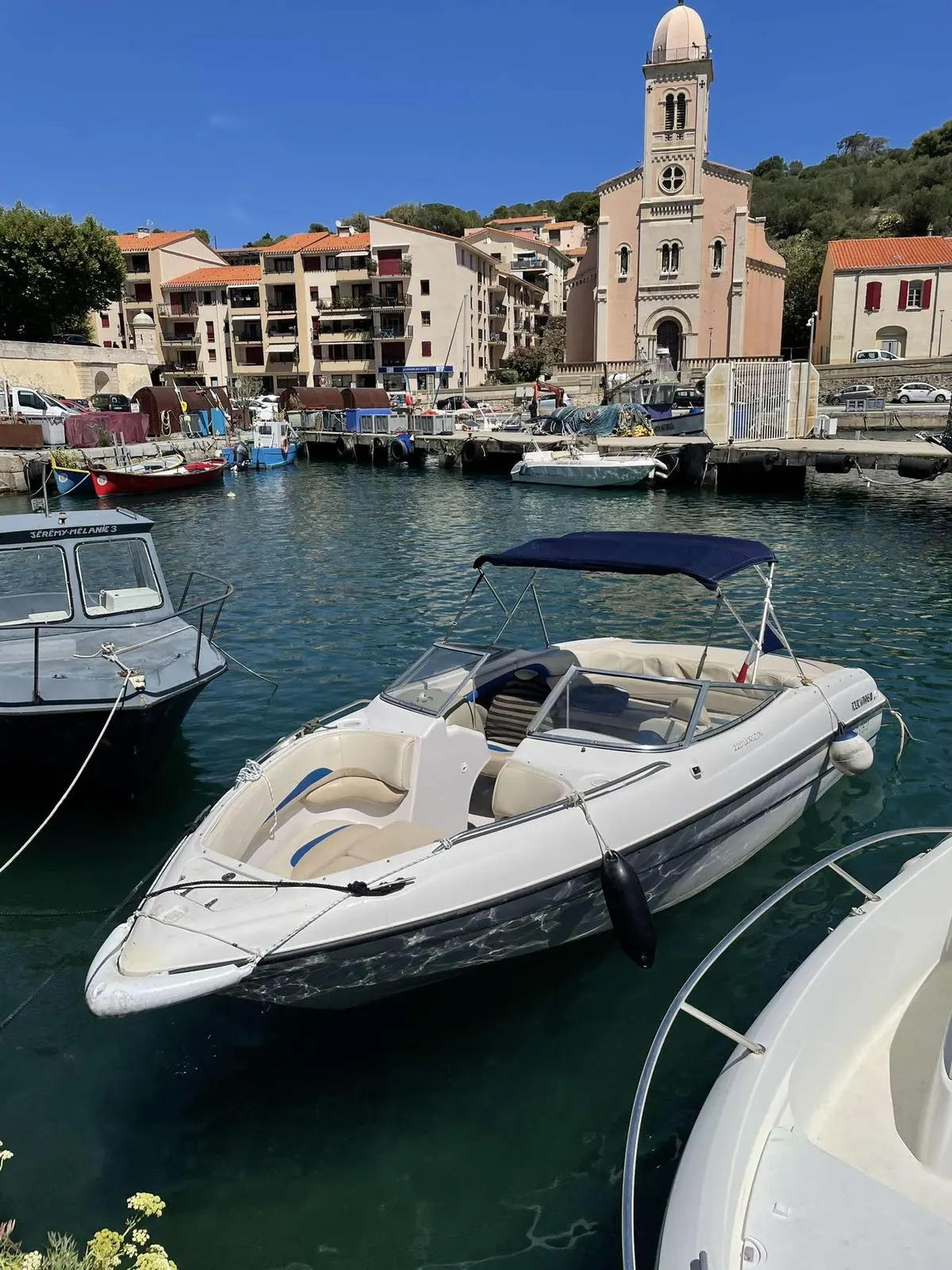 Four Winns Horizon 220 — Vedette blanche amarrée dans un port, avec cockpit ouvert et taud bleu.