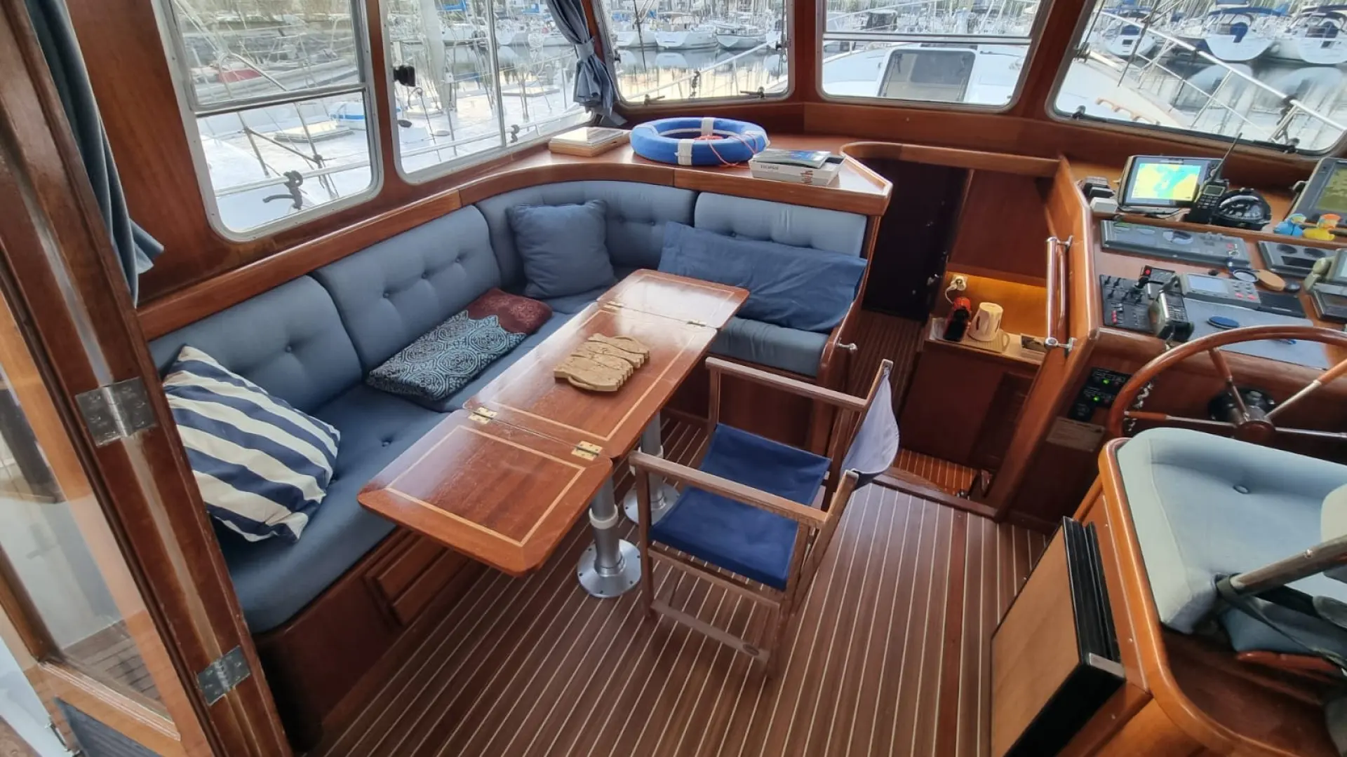Menorquin 150 — Carré intérieur en bois avec banquette, table et poste de pilotage.