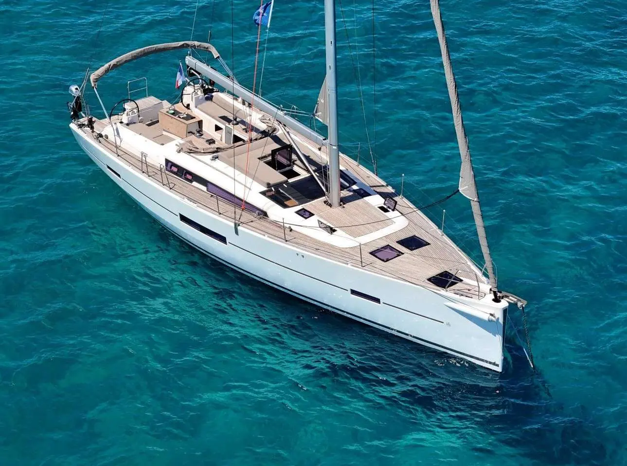 Dufour 500 Grand Large — Voilier blanc vu de trois quarts sur une mer turquoise.