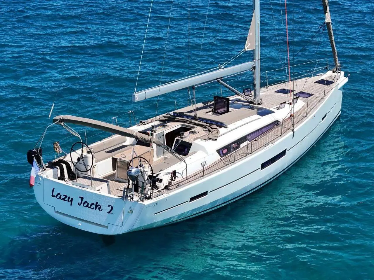 Dufour 500 Grand Large — Voilier blanc vu de trois quarts arrière sur une mer turquoise.