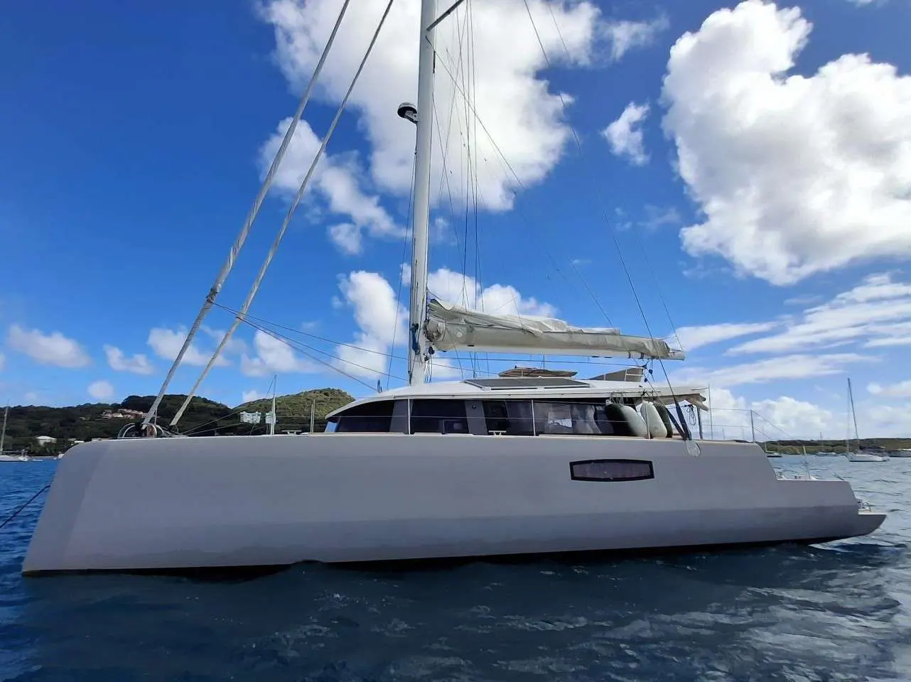 Neel Trimarans Neel 51 — Vue latérale d’un voilier multicoque blanc sur l’eau, sous un ciel nuageux.