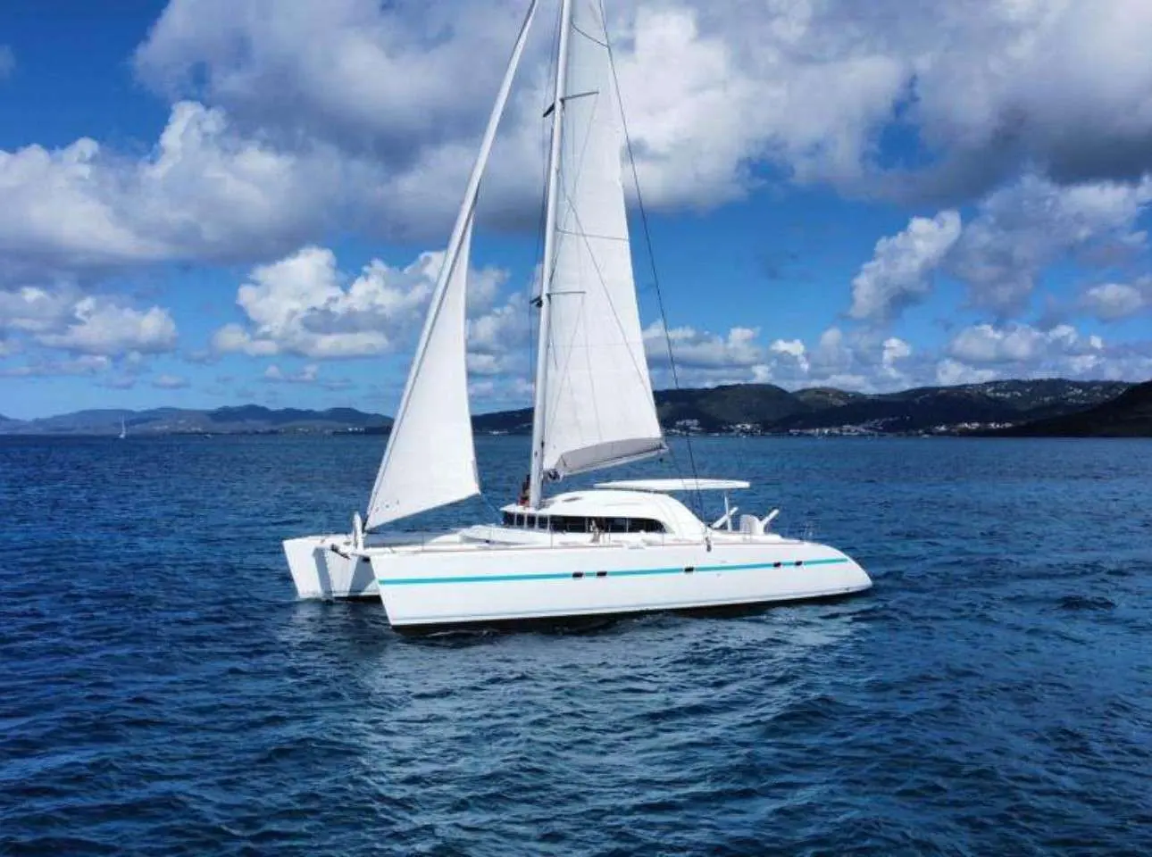 Lagoon 570 — Catamaran blanc naviguant toutes voiles dehors dans une baie tropicale.