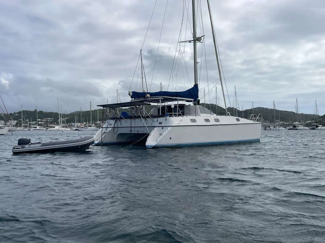 Jeantot Privilege 12 — Catamaran blanc à voile amarré dans une baie, avec une annexe à bâbord.