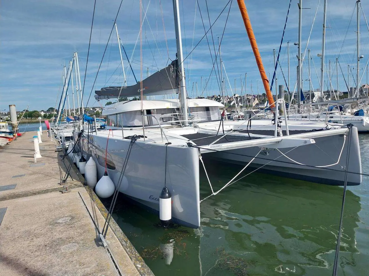 Excess Catamarans Excess 14 — Catamaran blanc amarré dans un port de plaisance, vu de trois quarts avant.