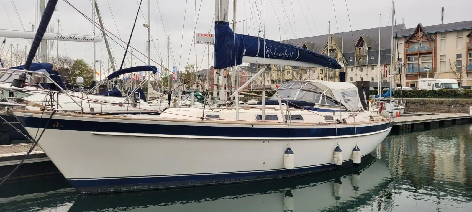 Hallberg Rassy 39 — Voilier blanc et bleu amarré dans un port, vu de profil côté tribord.
