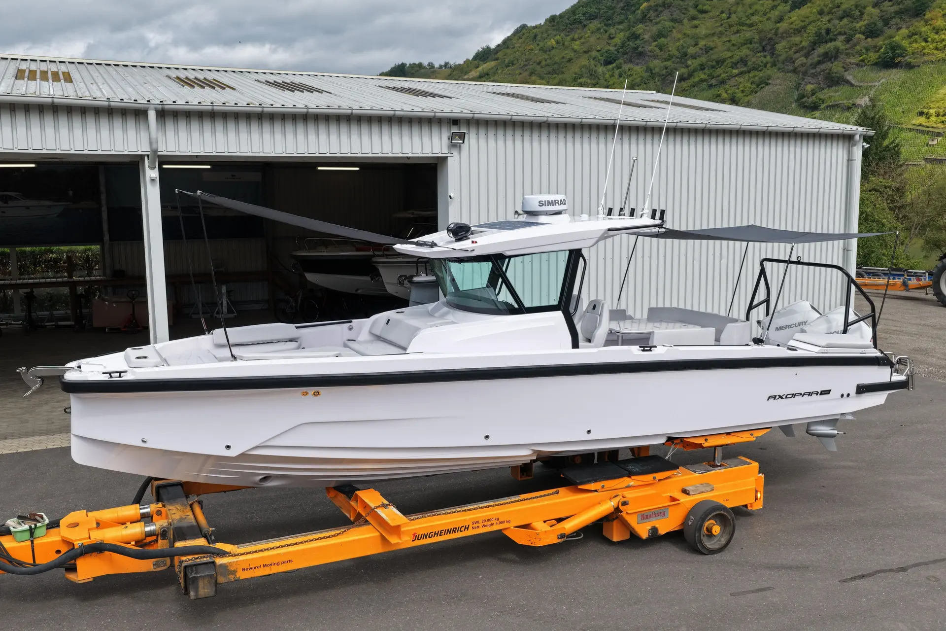 Axopar 29 CCX — Vue latérale d’un bateau blanc posé sur une remorque devant un hangar.