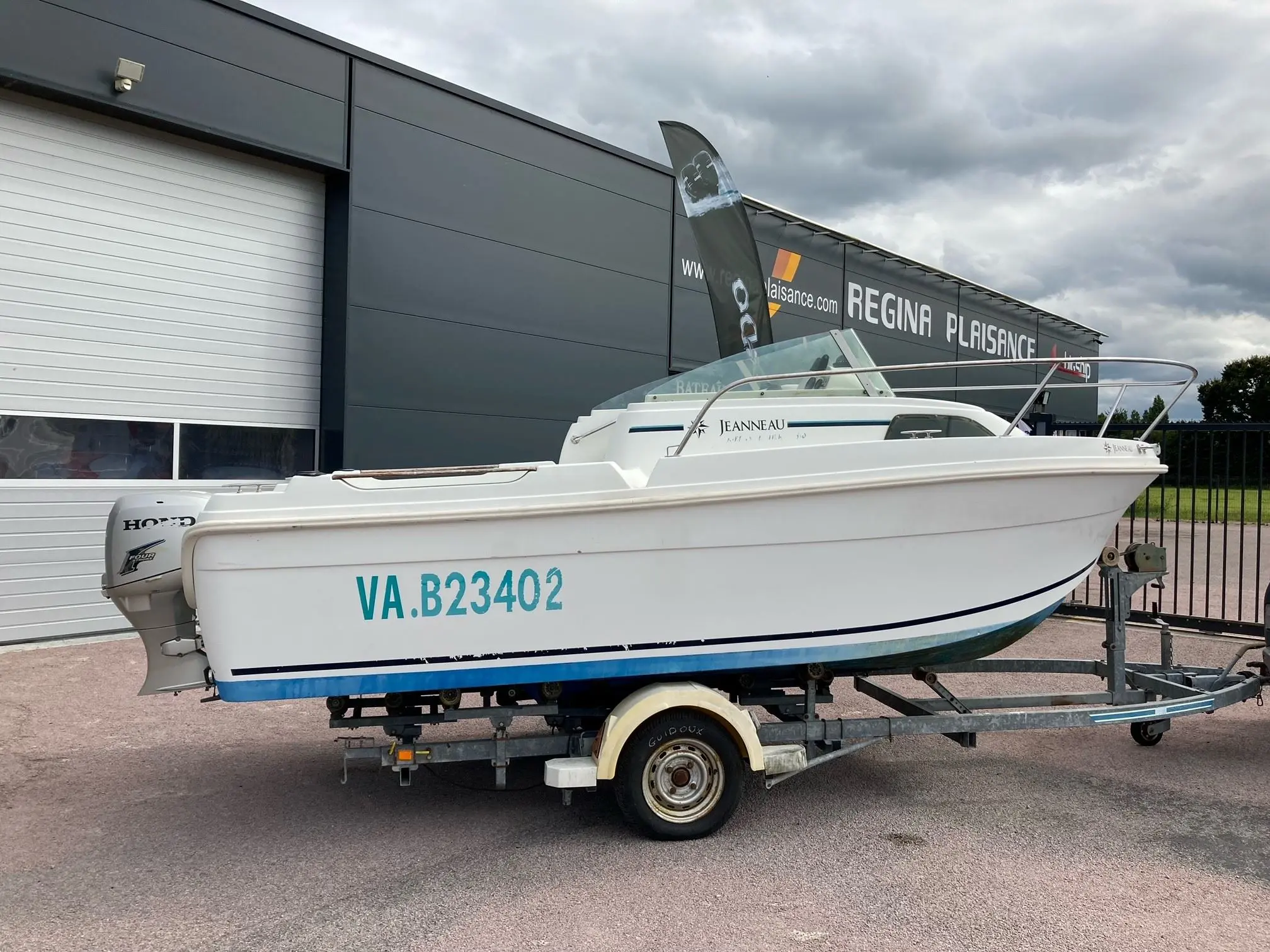 Jeanneau Merry Fisher 530 — Bateau à moteur blanc photographié sur une remorque devant un bâtiment professionnel.
