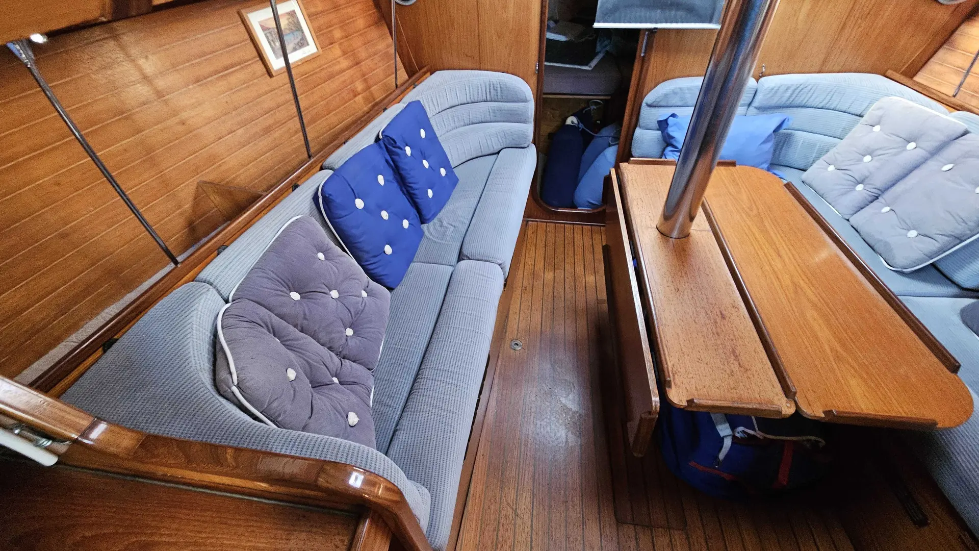 Jeanneau Sun Rise 35 — Vue du carré intérieur d’un voilier, avec banquettes et table en bois.