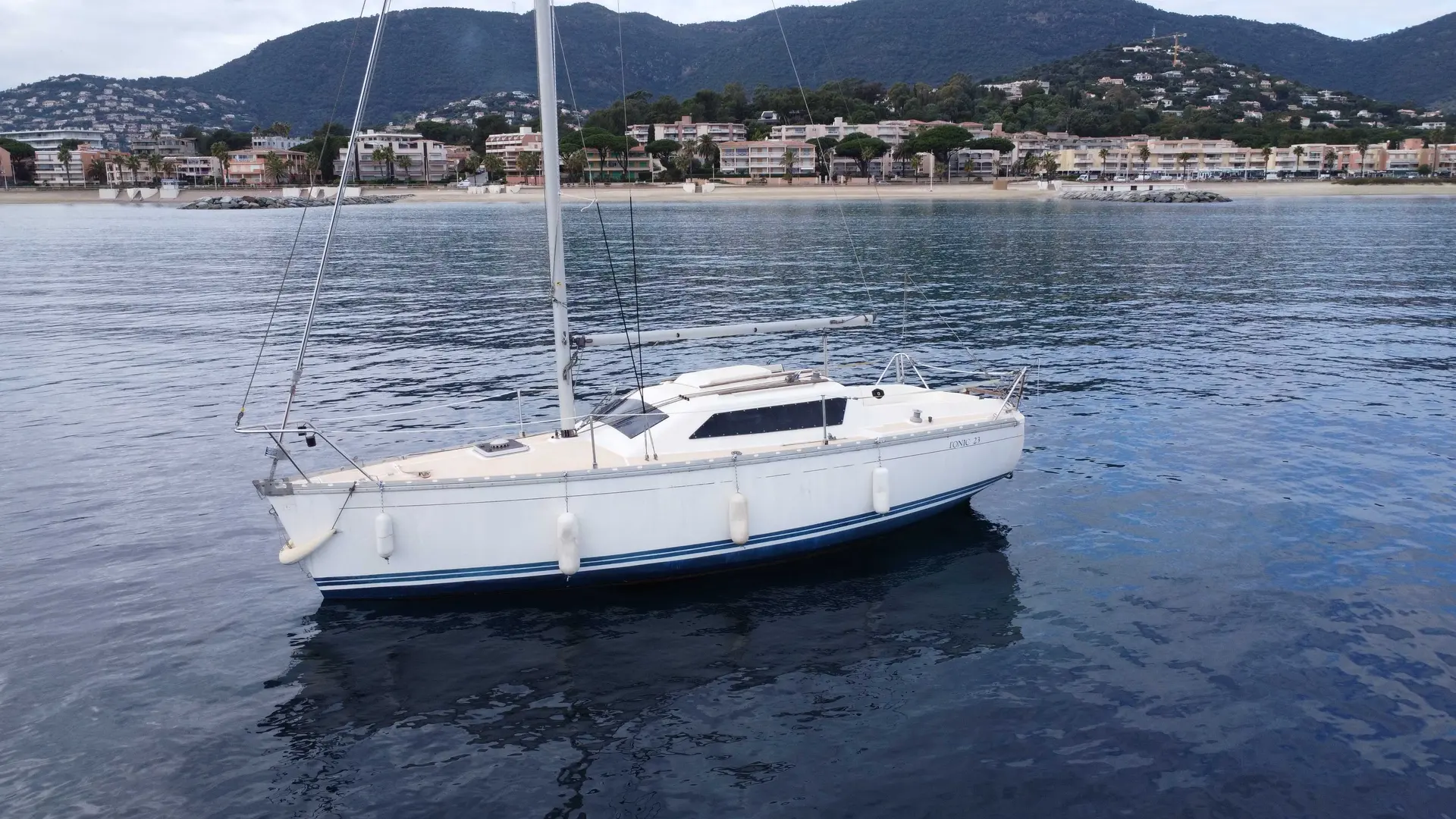 Jeanneau Tonic 23 — Voilier blanc photographié au mouillage devant une côte urbanisée.