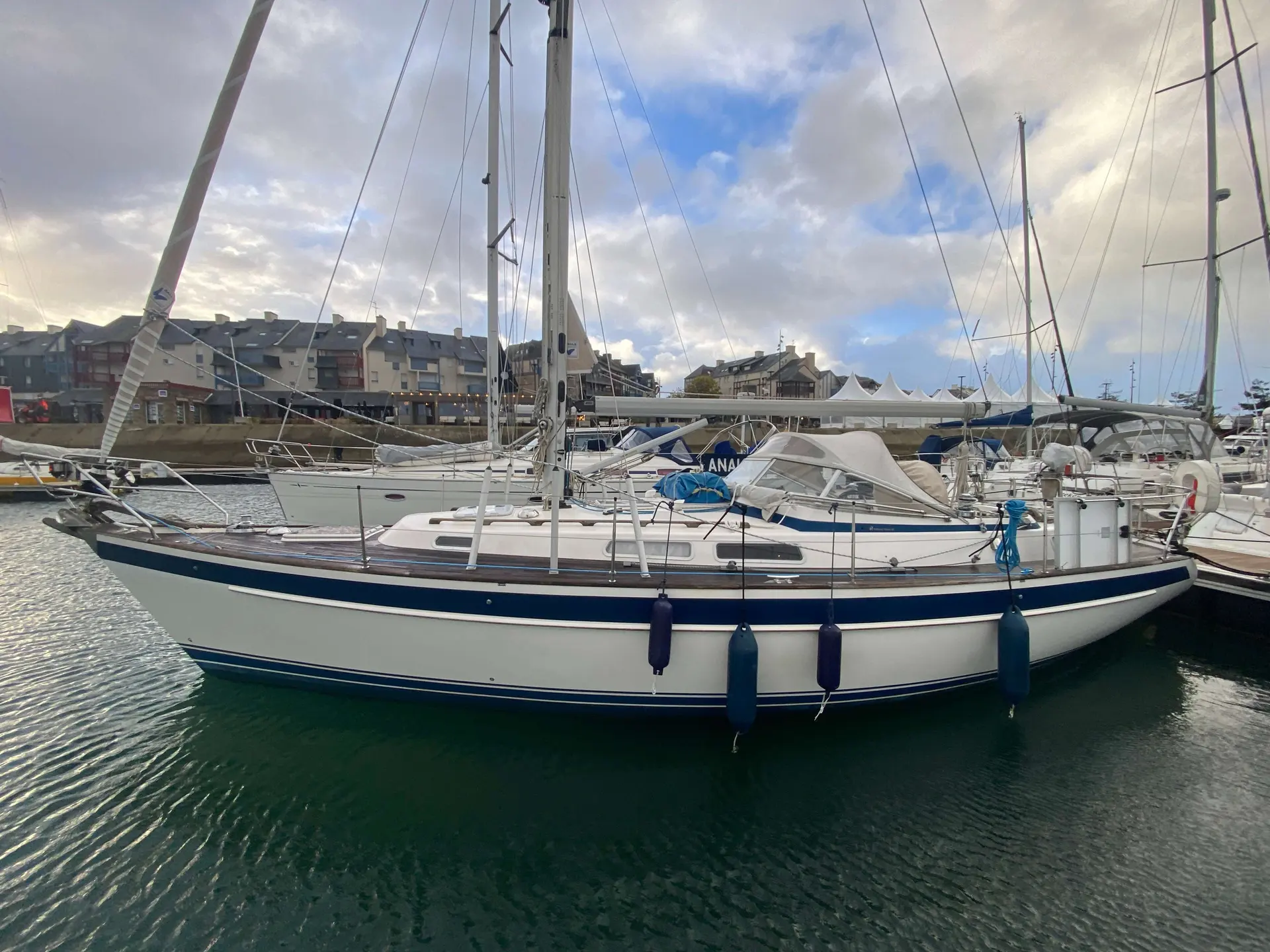 Hallberg Rassy 36 — Voilier blanc et bleu amarré dans un port, vu de profil.