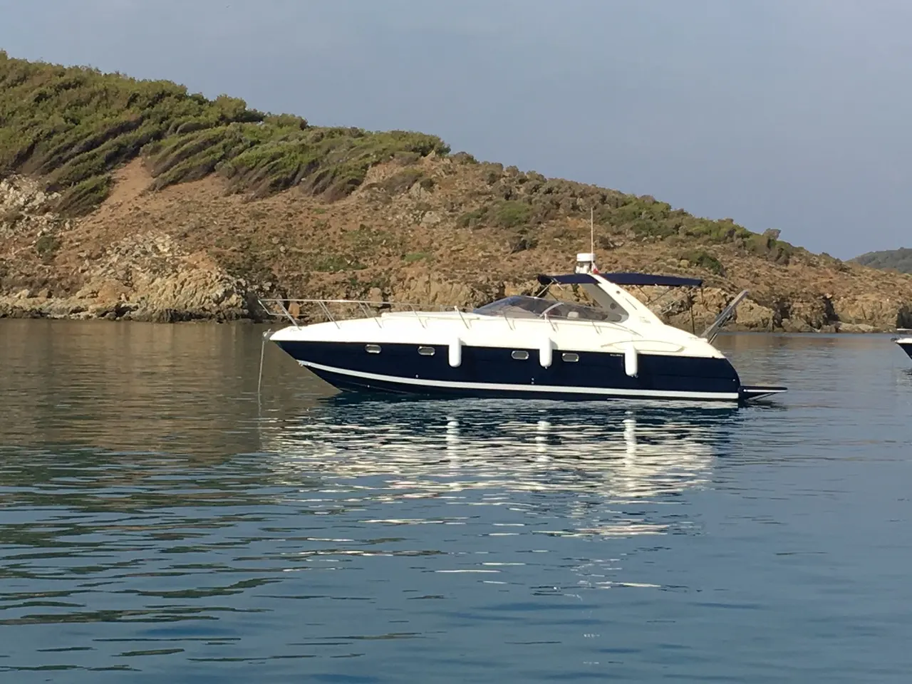 Airon Marine 388 — Bateau à moteur vu de profil, au mouillage devant une côte rocheuse.