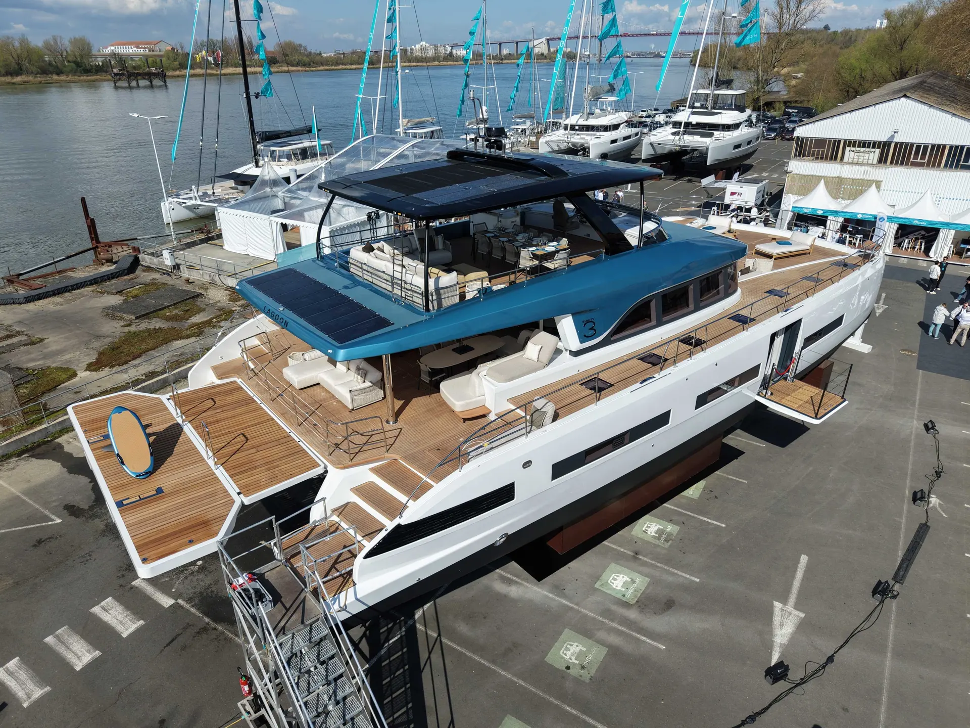 Lagoon Eighty 3 — Vue aérienne trois quarts d’un catamaran blanc et bleu exposé dans un port.